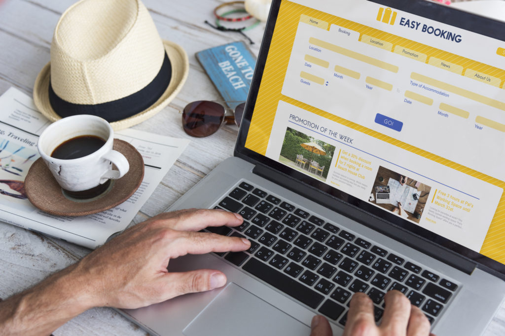 Online Buchungsplattform für Ferienwohnungen auf Laptop geöffnet, Sonnenhut und Kaffeee danebn