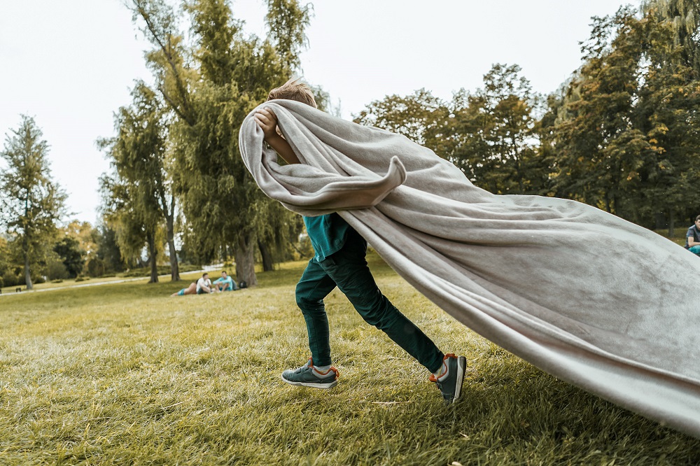 Kind rennt durch Garten einer Ferienwohnung mit einer Decke
