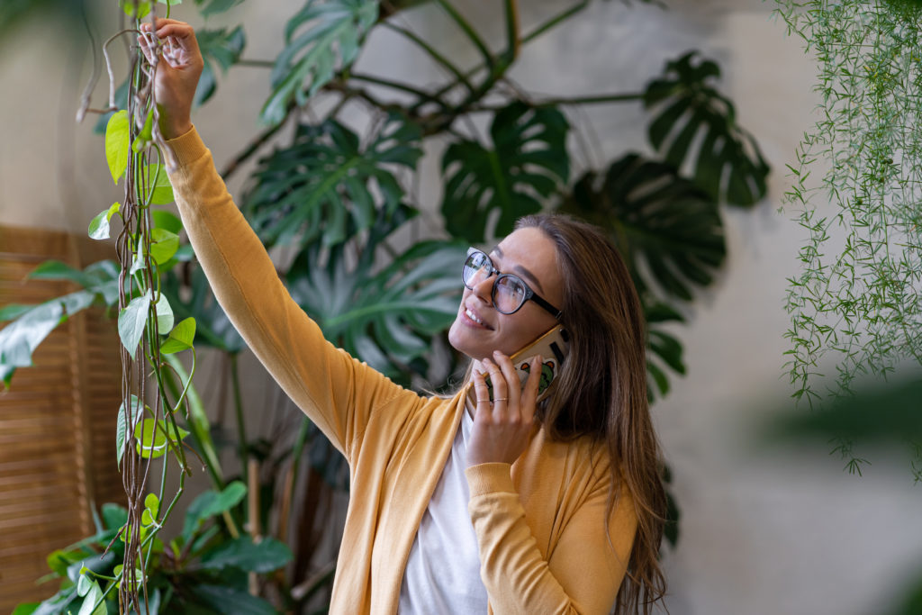 Ferienwohnung buchen, junge Frau nimmt telefonische Buchung entgegegen und pflegt dabei Wohnungspflanzen