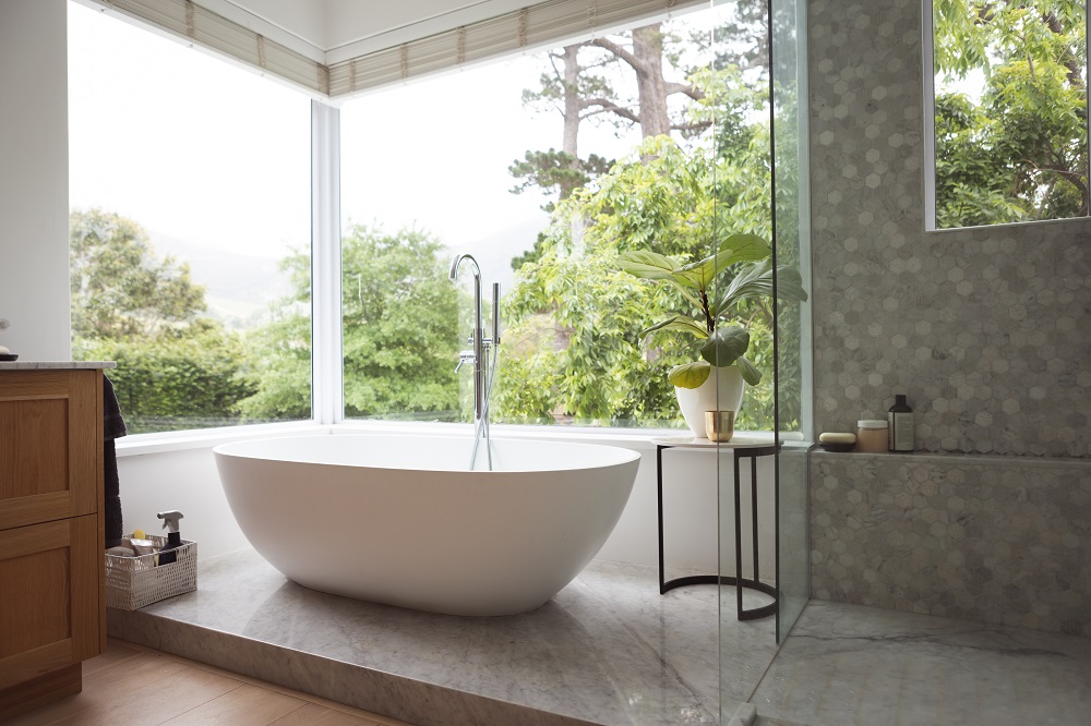 Modernes Badezimmer in einer Ferienwohnung, weißre freistehende Badewanne vor großer Fensterfront
